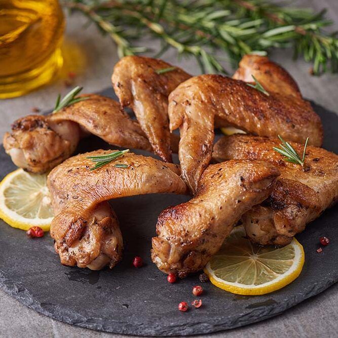 roasted-chicken-wings-barbecue-sauce-with-pepper-seeds-rosemary-salt-black-stone-plate-gray-stone-table-top-view-with-copy-space